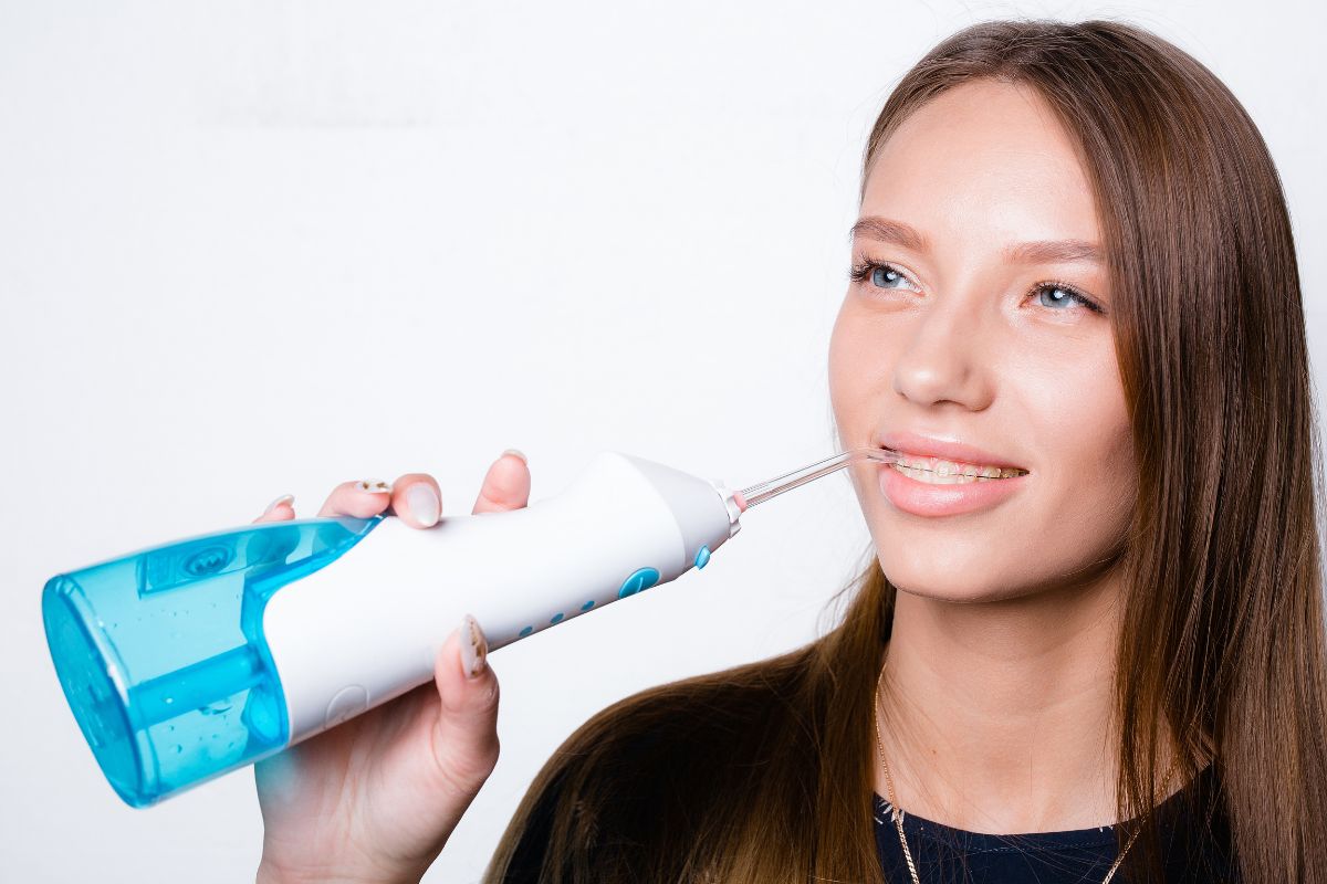 Top New Tools for Braces Woman demonstrating water flosser oral hygiene product against white background for dental care website.